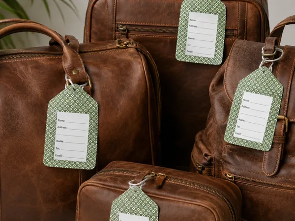 Green shweshwe luggage tags with name and address panels, attached to leather travel bags